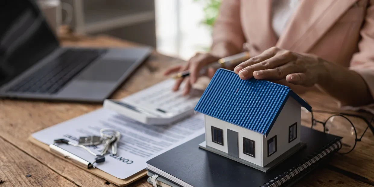 Real estate agent reviewing a contract with keys, a model house, and a laptop on a desk